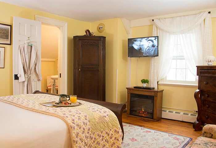 Inviting guestroom has butter-yellow walls with hardwood floors. Dark wood sleigh bed sits in front of fireplace