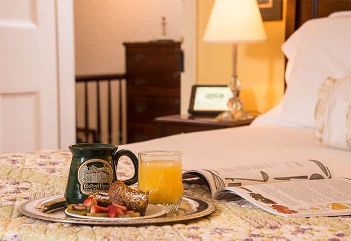 A silver tray holds coffee, orange juice, and fruit displayed on a neatly made bed