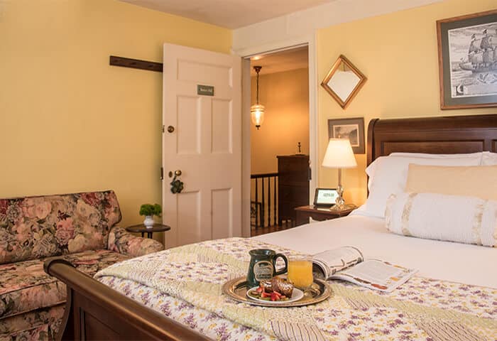 Inviting guestroom has butter-yellow walls with hardwood floors. Dark wood sleigh bed sits next to love seat