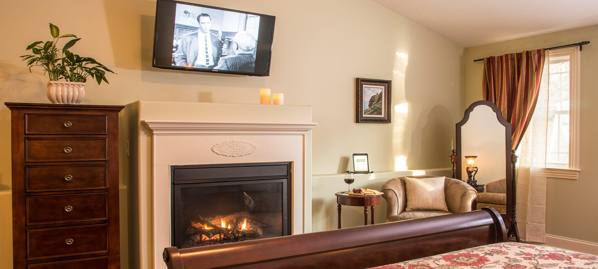 Guestroom features a roaring fireplace. Luxurious mahogany dresser sits next to wall-mounted television