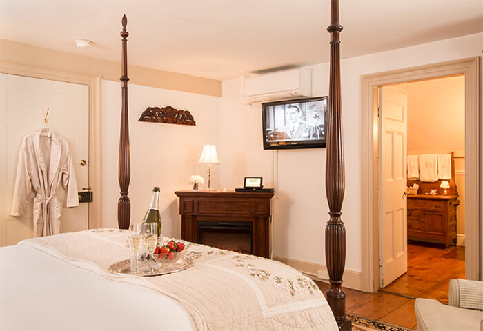 Guestroom features four post bed with a view of television and a corner fireplace