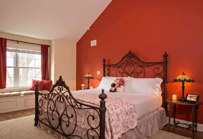 Cream colored bedroom with a red feature wall; featuring white linen bedding with floral quilt