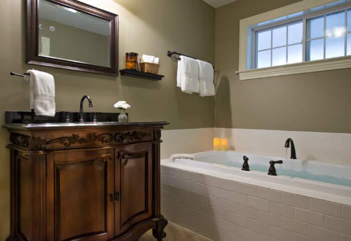 Moss green walled bathroom with dark wooden vanity and cream tiled tub