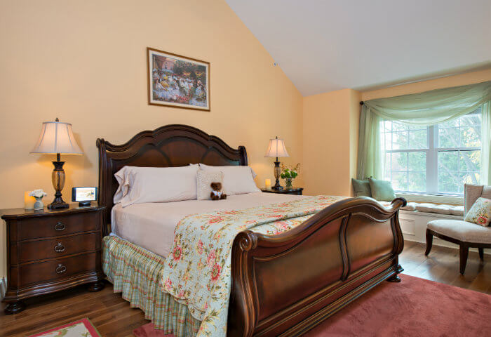 Bedroom with yellow walls has dark wooden furniture and bright white bedding with a floral quilt