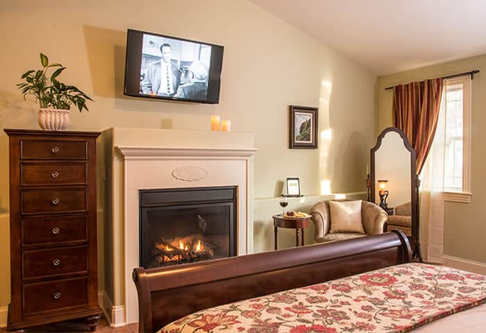 Guestroom features a roaring fireplace. Luxurious mahogany dresser sits next to wall-mounted television