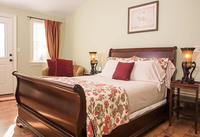 Guestroom displays soft green wall colors with hardwood floors and mahogany sleighbed; bedding is florals with cream