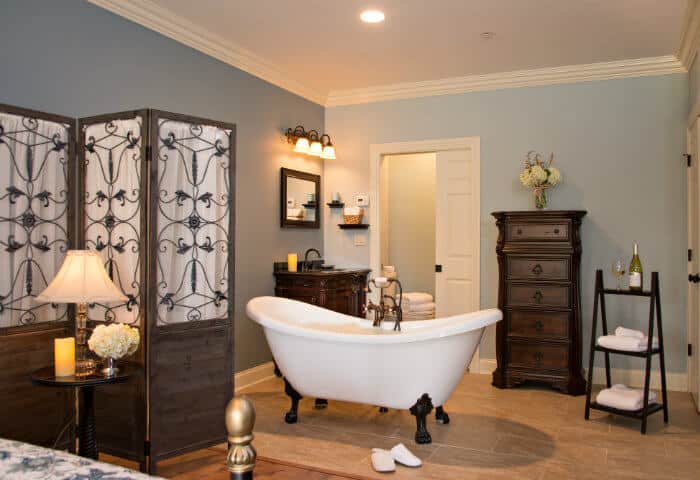 Sage blue bathroom featuring antique white clawfoot tub and dark wooden furniture