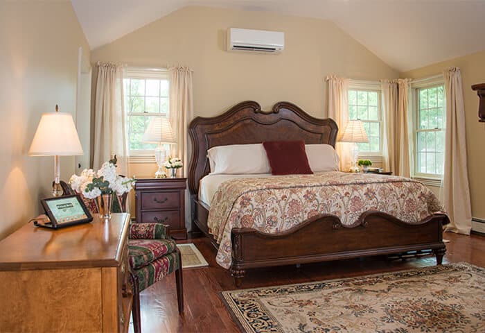 Charming bedroom with cream walls and wood flooring, features neatly made bed with quilt; also a cozy soft rug underfoot