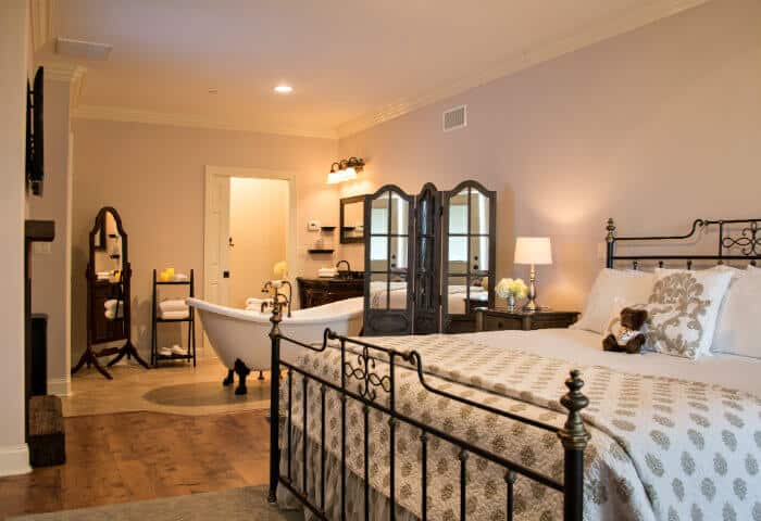 Cream walled en-suite featuring metal bedframe with white linens and antique white clawfoot tub