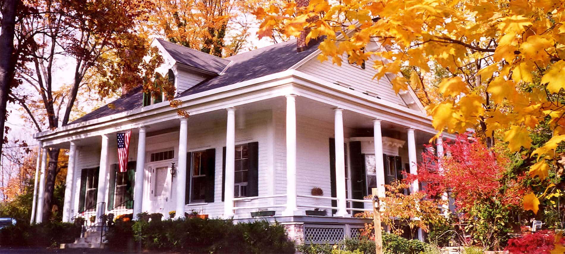 Exterior view of charming white house with numerous windows, sits among yellow and red trees of fall