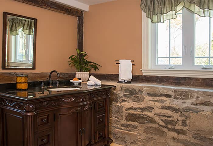 Bathroom has stonewall feature with gold wall color and dark wood vanity with mirror