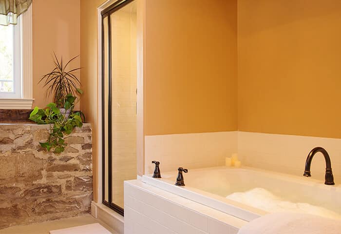 Bathroom has stonewall feature with gold wall color and white bathtub; displays spa amenities