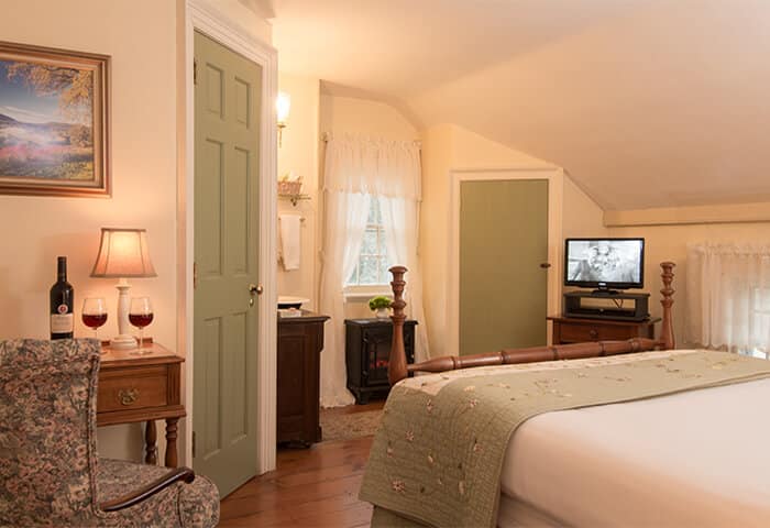 Charming bedroom with cream walls and green trim, features neatly-made bed with quilt; tv and comfy chair to the side