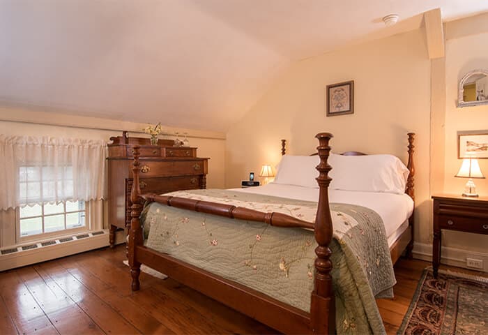 Charming bedroom with cream walls and wood flooring, features neatly made bed with quilt; also a cozy soft rug underfoot