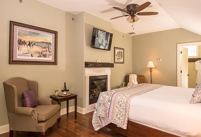 Inviting guestroom features a warm fireplace with two charming sitting areas; walls are in soft moss green, floors are hardwood