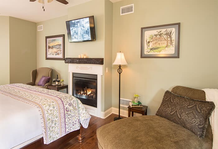 Inviting guestroom features a warm fireplace with two charming sitting areas; walls are in soft moss green, floors are hardwood