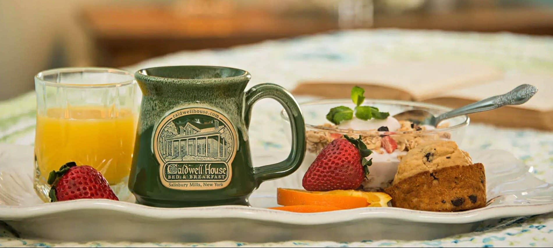 White plate with a glass of orange juice, green pottery mug, fruit and slice of cake