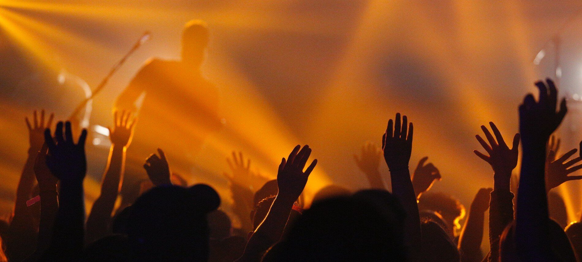 A crowd of people with hands raised in front of a stage with orange lightings and fog