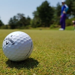 White golf ball sitting on a green with a blurred golfer standing in background