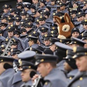 A large group of military cadets in dark blue uniforms and black hats with a mascot in their midst