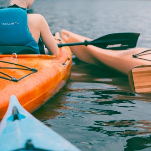 Person in a blue lifejacket sitting in an orange kayak out on the water