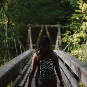 Woman wearing a backpack walking down a long wooden bridge in a forest