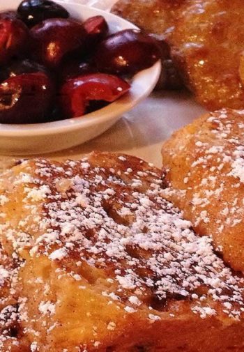 Slices of thick french toast on a white plate with a berry compote on the side,