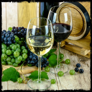 Two glasses of wine, one red and one white, in front of a barrel and grapes