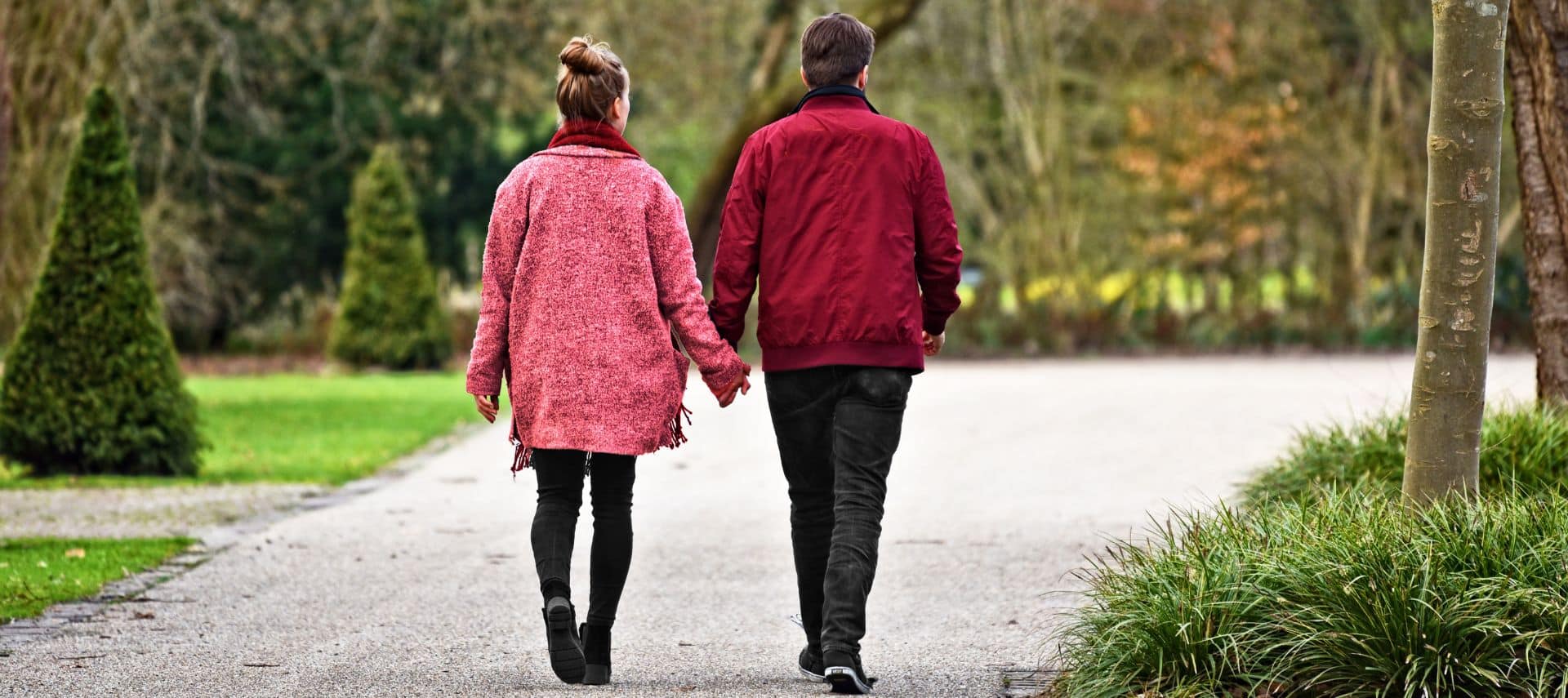 romantic couple holding hands while walking through a park during autumn