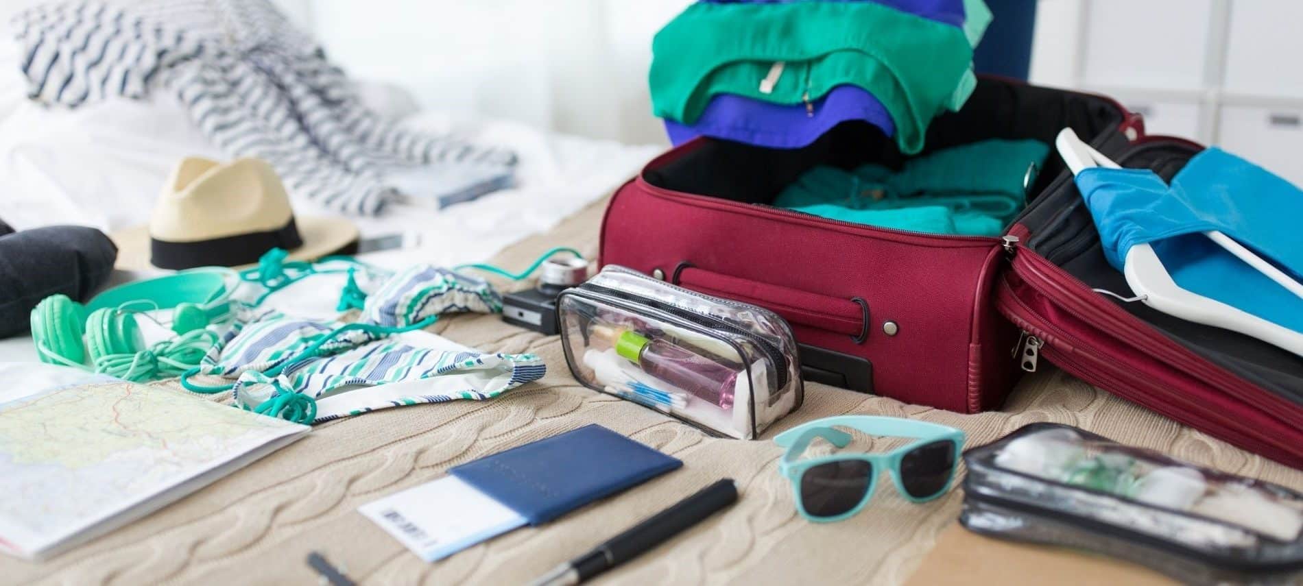 Open suitcase on a bed with multiple items ready to pack