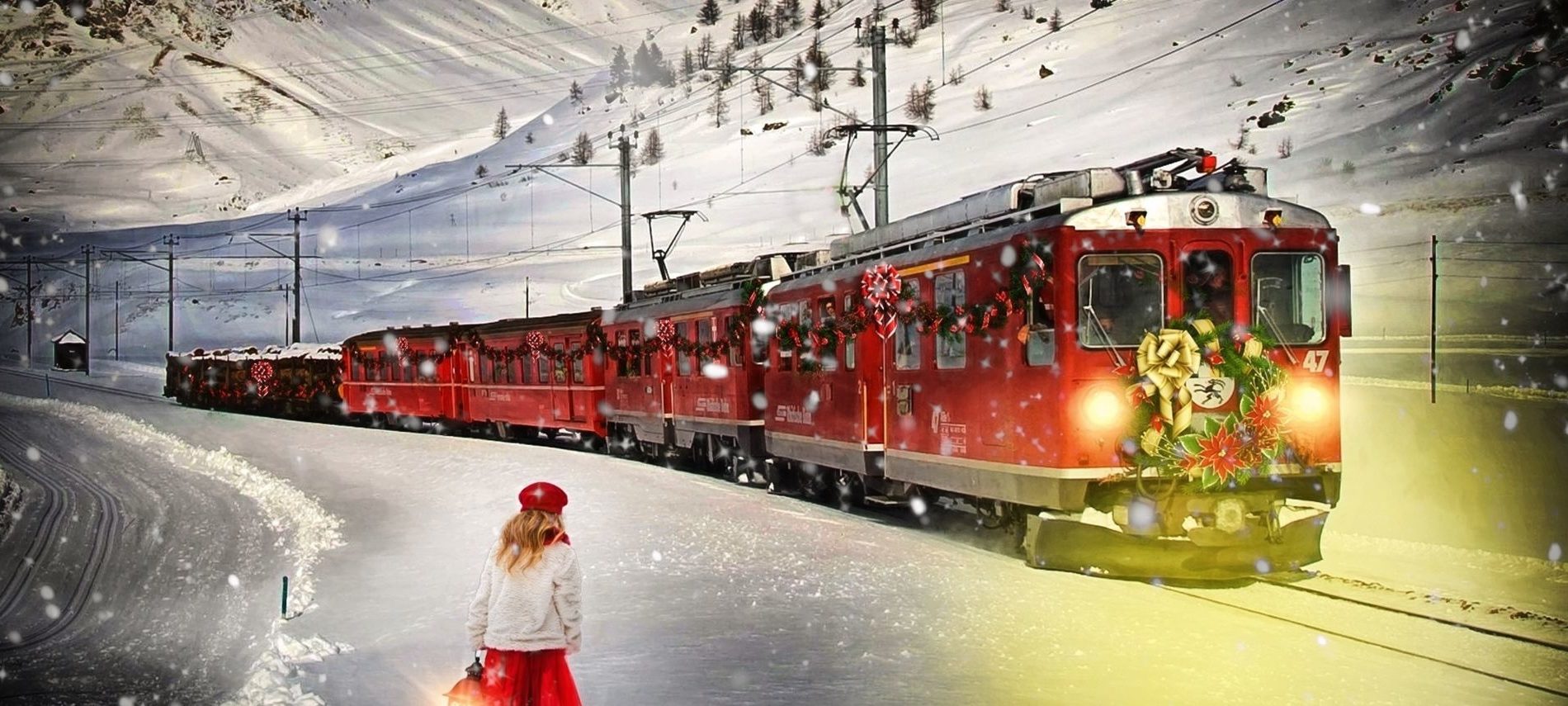 Red vintage train with Christmas decorations in front, with snow coming down. Small girl with red beret and red dress over snow parka waiting for train.