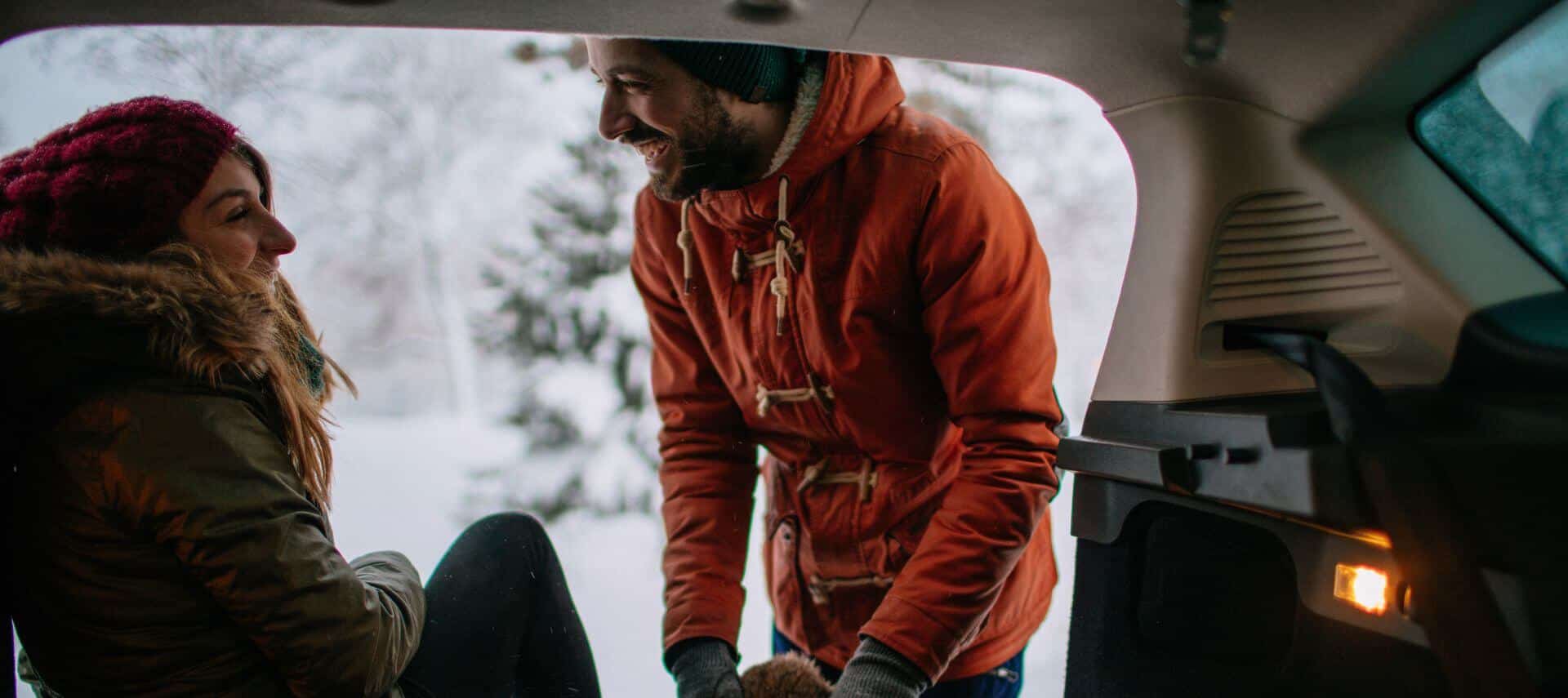 smiling romantic couple in winter at the rear of an open-hatched car