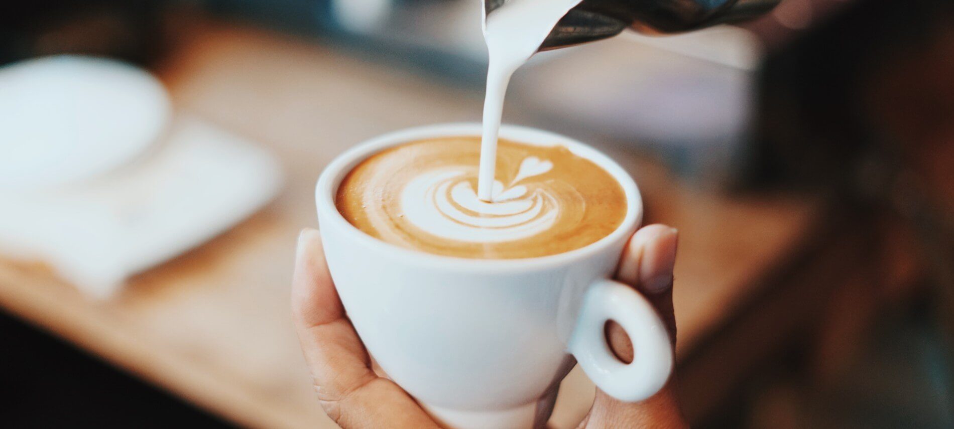 White milk being poured into a mug full of cappuccino coffee