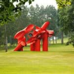 Large red sculpture in the middle of a wooded area 