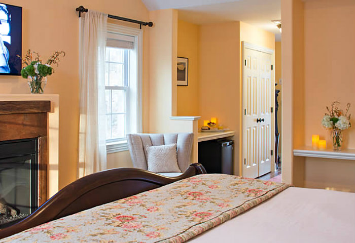 Floral quilt at the foot of a queen bed with dark wood footboard facing a fireplace and flat screen tv