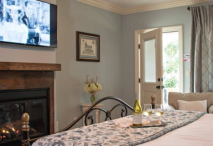 Neatly made queen bed in front of a fireplace and flat screen tv, with a tray of wine and cheese