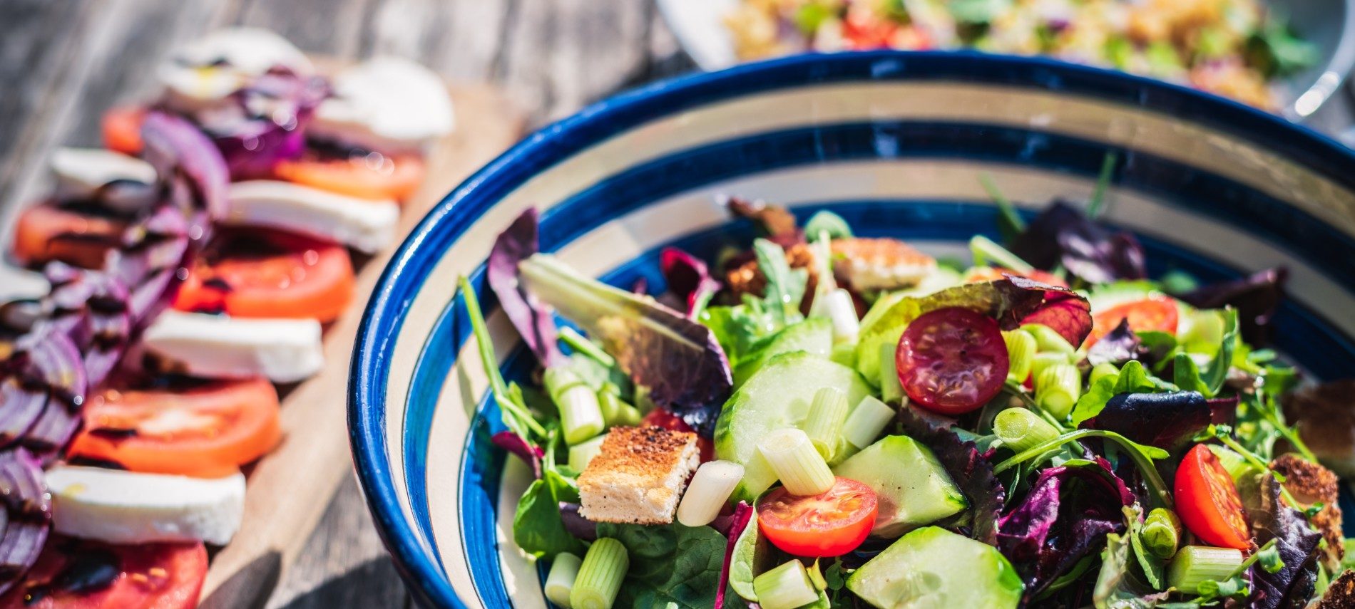 Large blue and white bowl full of greens and vegetables next to platter of tomatoes and mozzarella slices