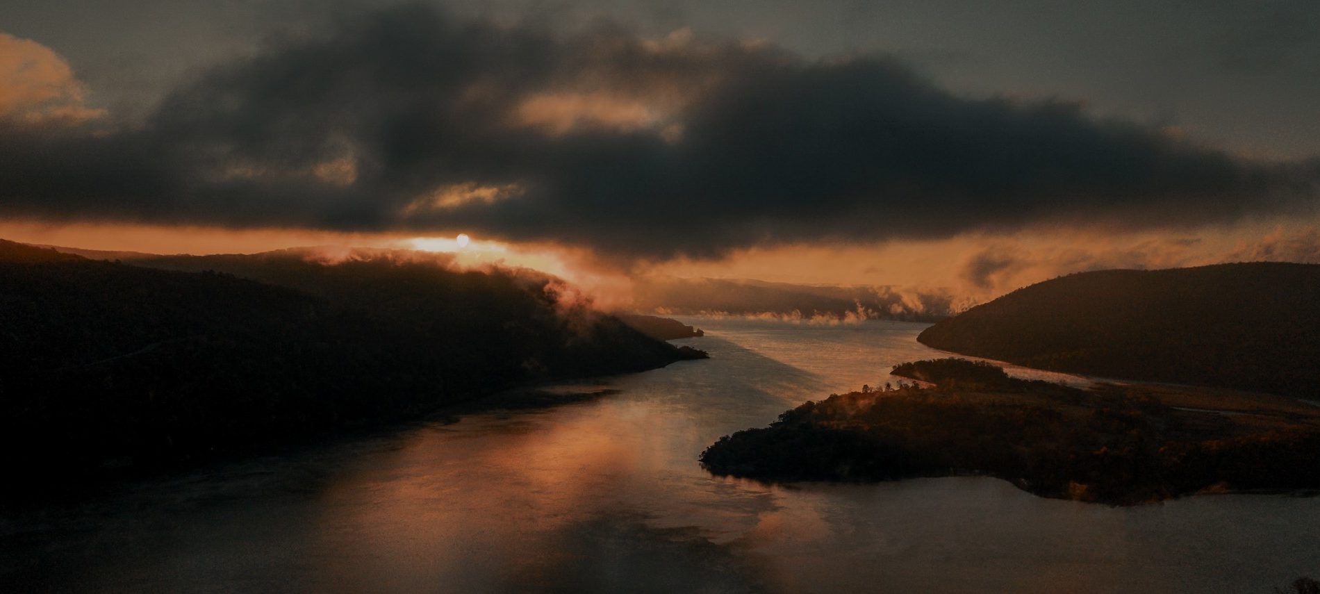 Overlooking a big valley with a river from on top of a mountain with sunset skies above