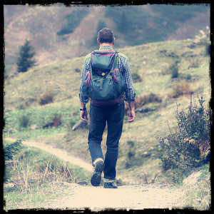 Lone male hiker wearing a green backpack walking on a dirt trail