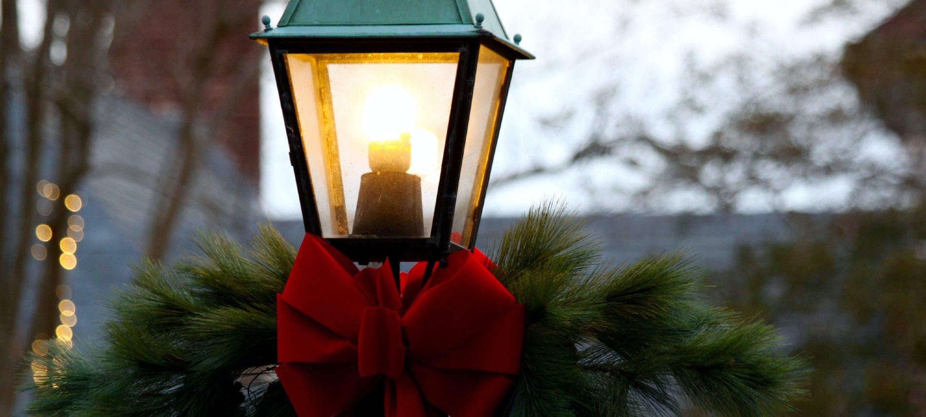 One tall black lantern lit up with greenery and a red bow at the base