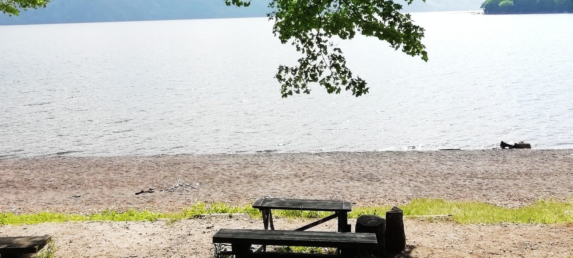 Wooden picnic bench on a deserted beach area in front of large body of water