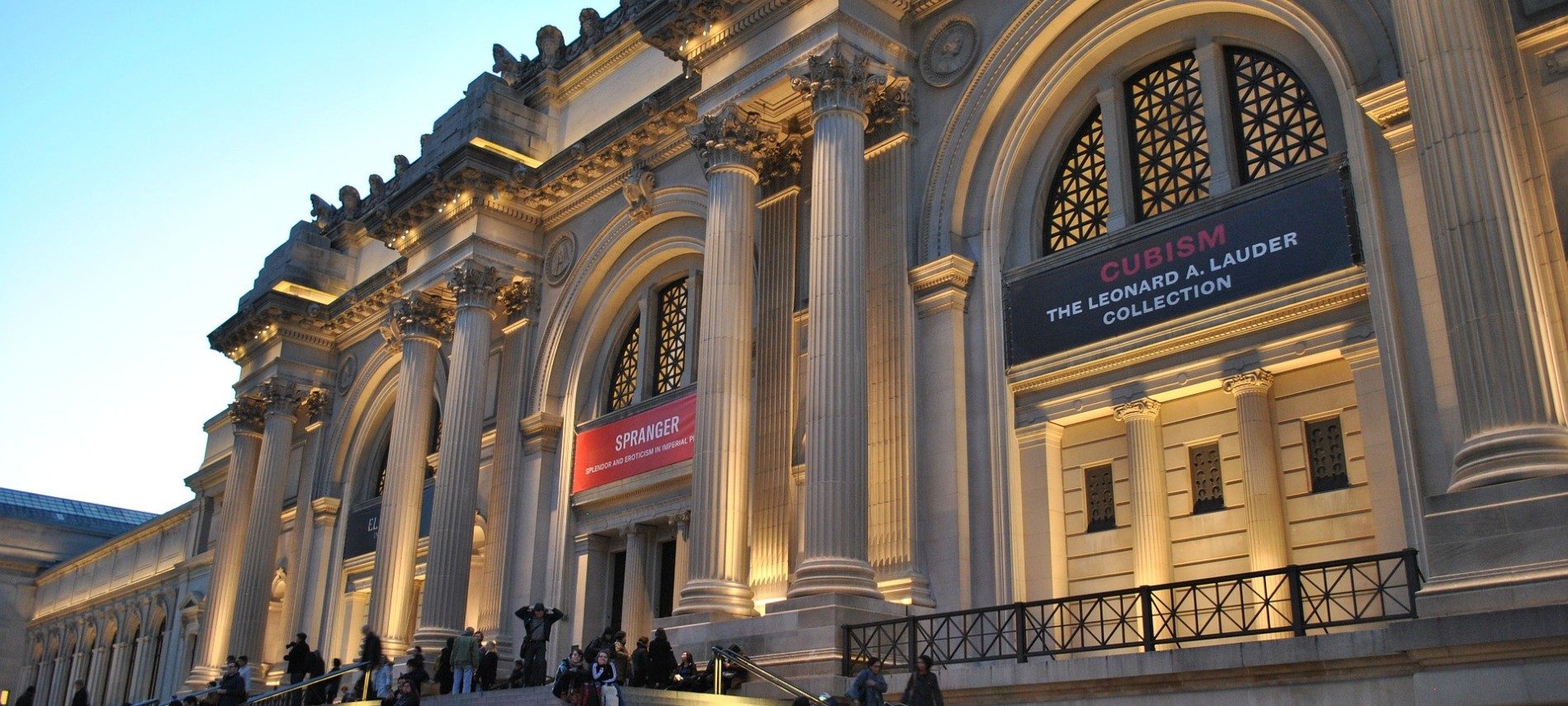 Front facade of large museum of art with tall columns, arches, and wide steps with people mingling