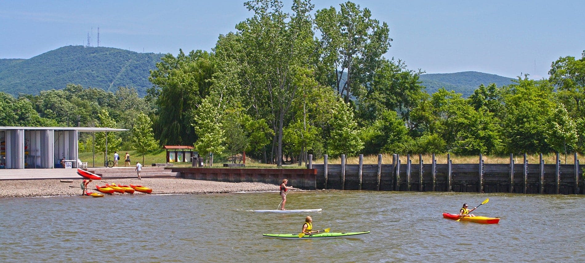 Small cove of water with a beach, white building, wood wall and kayakers in the water