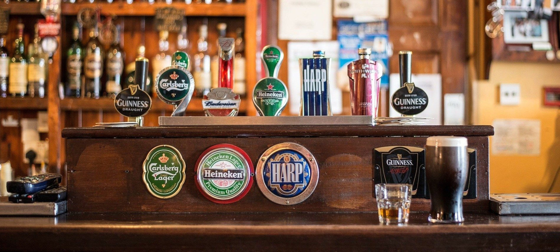 Inside of a pub showing a bar counter with seven different beers on tap and a couple glasses of beer on the table