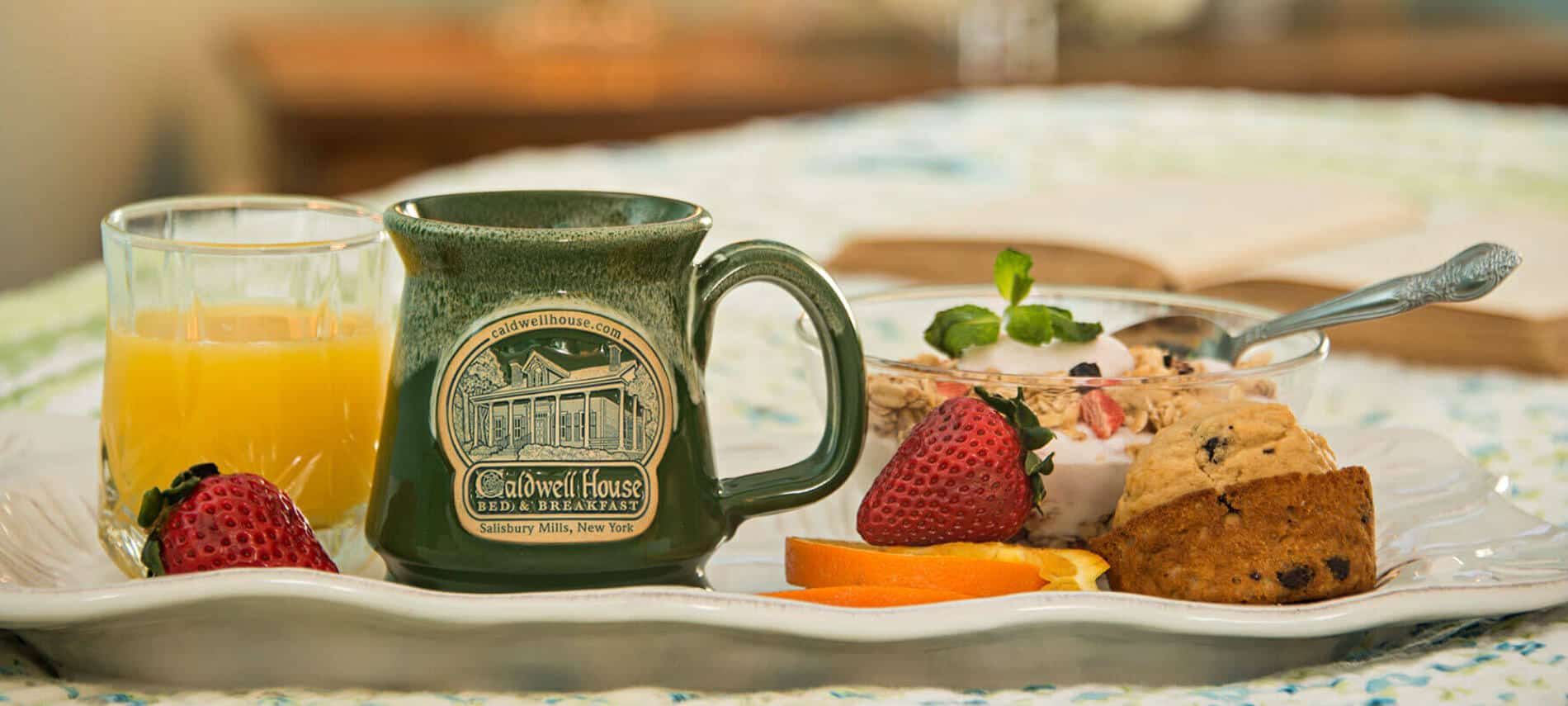 Closeup of white tray with Caldwell House mug, fruit, muffin and glass of orange juice