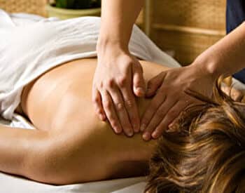 Women laying face down on table with white towel drapped over getting a message.