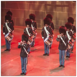 A group of military tattoo musicians in uniform on stage playing trumpets and drums