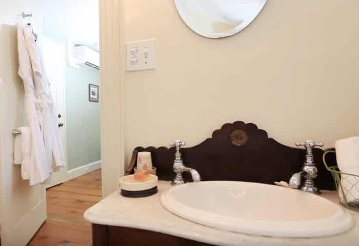 Dark wood bathroom vanity with white sink looking into the attached bedroom