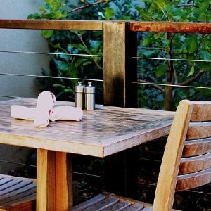 One table with two light wood chairs on a patio next to a green tree