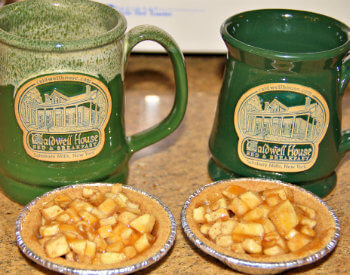 Two green pottery coffee mugs with Caldwell House emblem and two petite individual size apple pies.